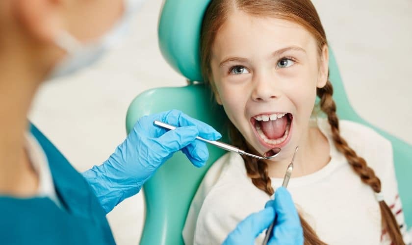 Young girl with braids smiling during dental examination in treatment chair.