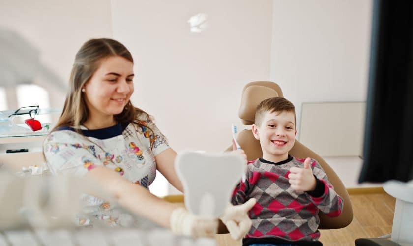 Young pediatric dental patient smiling in dental chair with female dentist during examination.