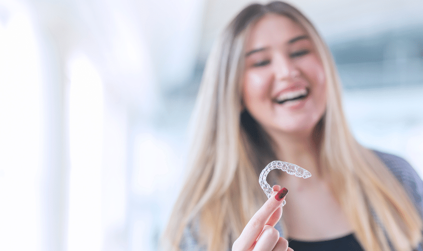 Teenage girl smiling while holding an Invisalign clear aligner tray in Englewood.