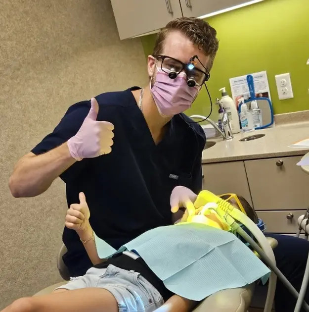 Dentist giving thumbs up while holding yellow dental materials during new patient appointment.