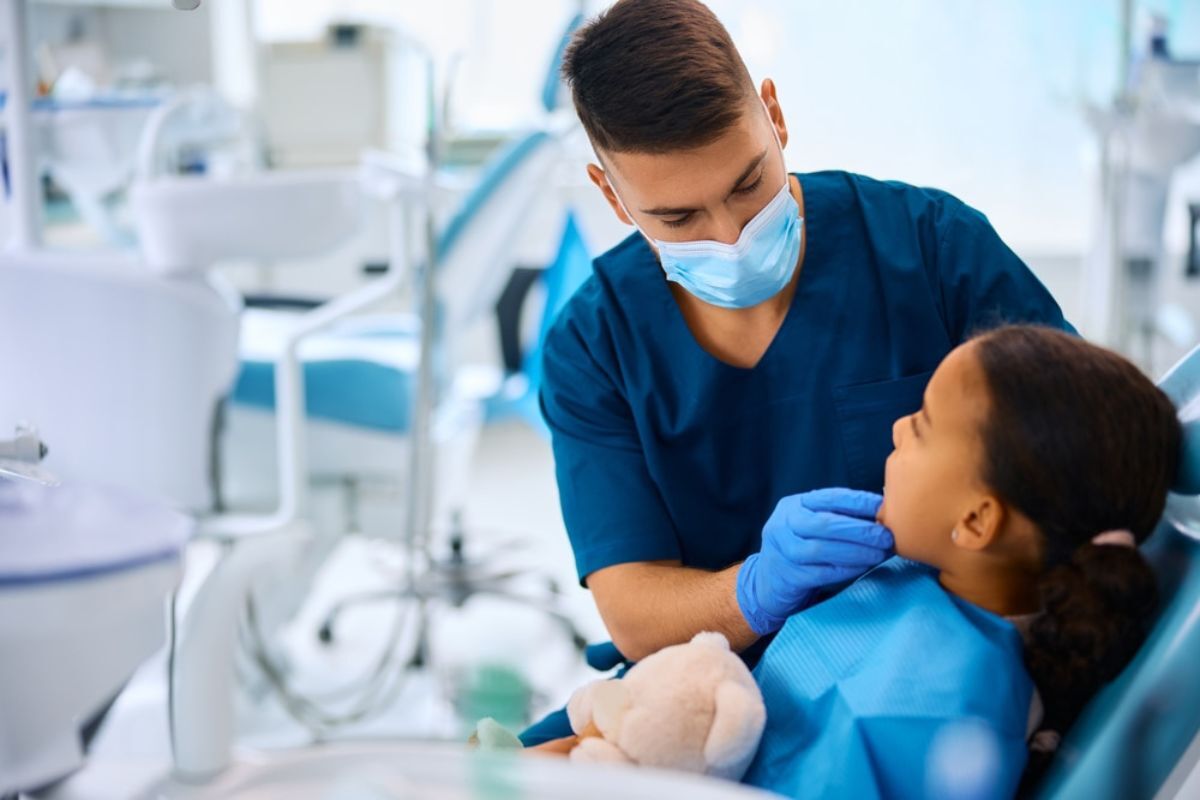 Young dentist examining pediatric patient in modern dental office treatment room.