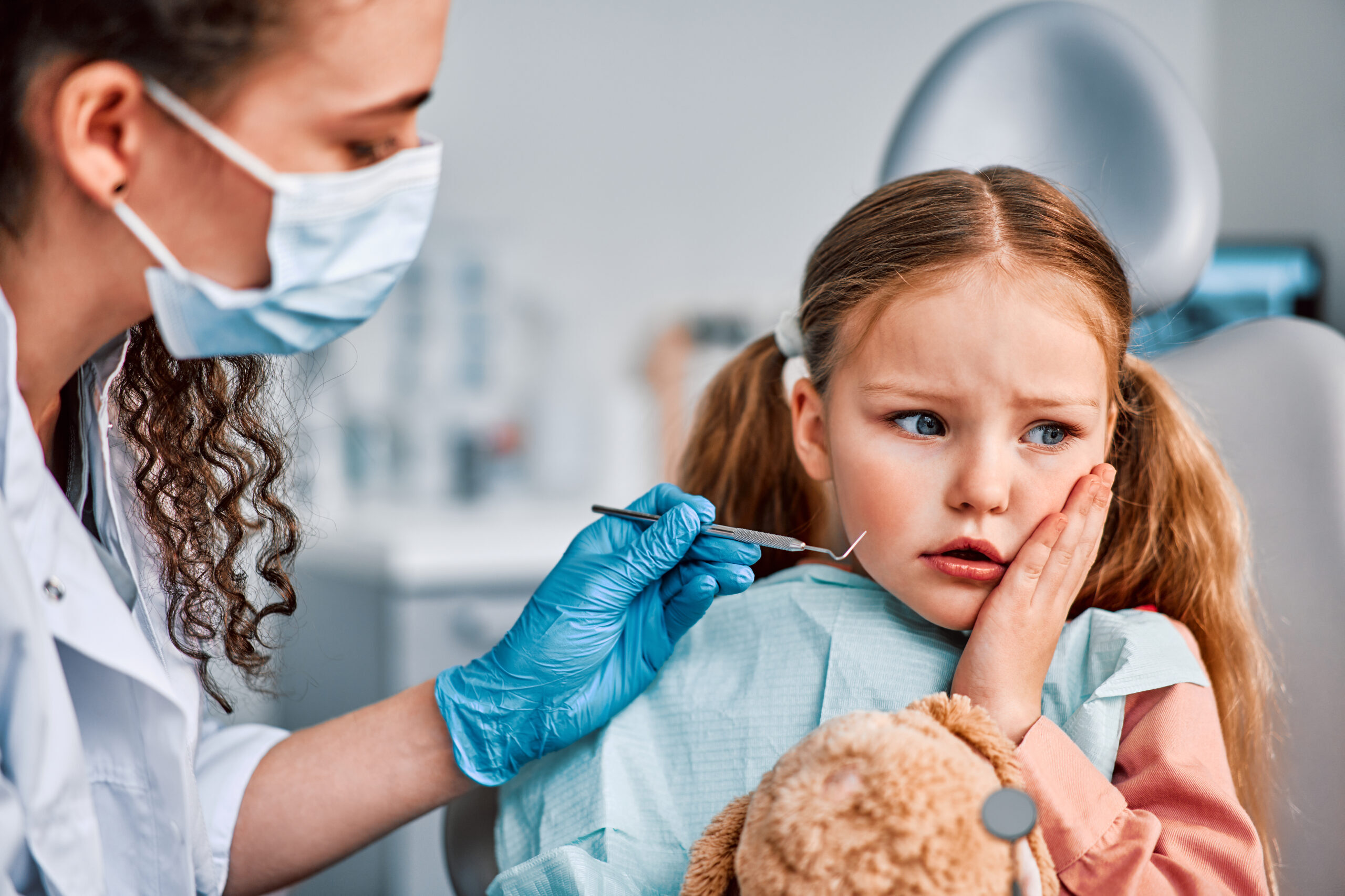 Anxious child at dentist appointment while hygienist examines teeth with dental tools.