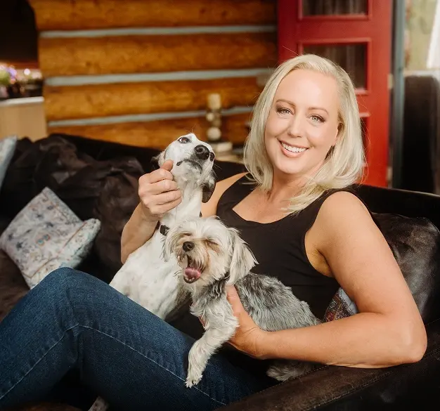 Dr. Heather Jenkins smiles with two small dogs on a couch in her Englewood dental office.