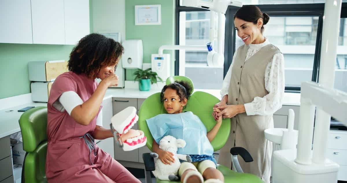 Young child in dental chair with dentist and parent during first dental visit examination.